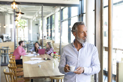 Mature businessman in a cafe with colleagues having a meeting in background - FKF03712