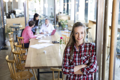 Porträt einer lässigen Geschäftsfrau in einem Café mit Kollegen, die im Hintergrund eine Besprechung abhalten - FKF03713