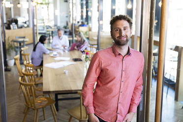 Portrait of casual businessman in a cafe with colleagues having a meeting in background - FKF03714