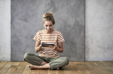 Smiling young woman sitting on the floor using a digital tablet - FMKF06037