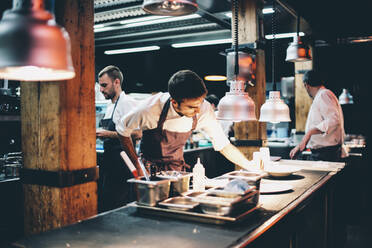 Koch, der in der Küche eines Restaurants das Essen auf einem Teller serviert - OCMF00852