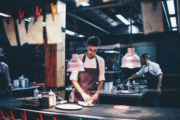 Koch, der in der Küche eines Restaurants das Essen auf einem Teller serviert - OCMF00856