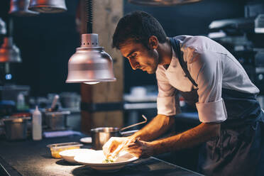 Cook serving food on a plate in the kitchen of a restaurant - OCMF00863