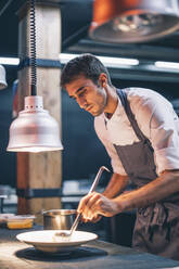 Koch, der in der Küche eines Restaurants das Essen auf einem Teller serviert - OCMF00864