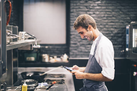 Lächelnder Koch mit Smartphone in der Küche eines Restaurants, lizenzfreies Stockfoto