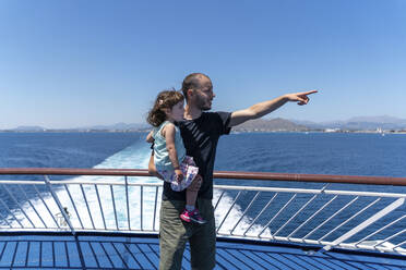 Vater steht auf dem Deck eines Schiffes mit seiner kleinen Tochter auf dem Arm und zeigt in die Ferne, Mallorca, Spanien - GEMF03255