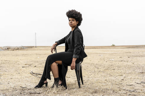 Porträt einer jungen, schwarz gekleideten Frau, die in einer düsteren Landschaft sitzt - ERRF01910