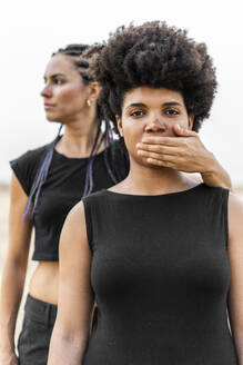 Woman's hand covering mouth of another woman - ERRF01918