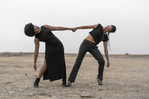 Two women dressed in black performing in bleak landscape - ERRF01930
