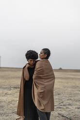 Zwei Frauen stehen in trostloser Landschaft und teilen sich eine Decke - ERRF01967