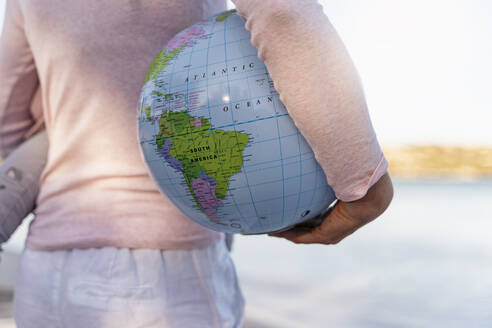 Back view of woman holding Earth beach ball under her arm, close-up - DIGF08828