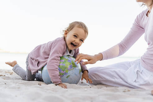 Porträt eines glücklichen kleinen Mädchens, das mit einem Strandball aus Erde am Strand spielt - DIGF08831