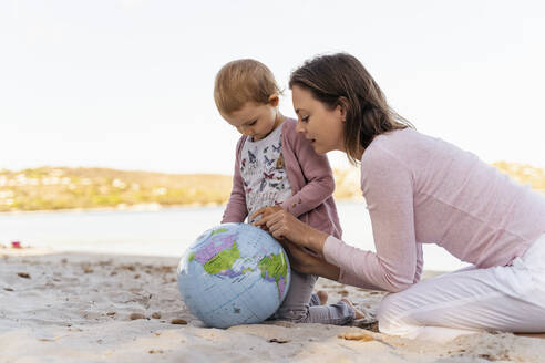 Mother and little daughter on the beach looking together at Earth beach ball - DIGF08839