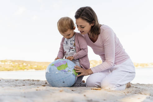 Mother and little daughter on the beach looking together at Earth beach ball - DIGF08840