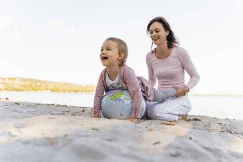 Mother and little daughter playing together with Earth beach ball at seashore - DIGF08841