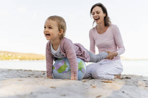 Mutter und kleine Tochter spielen zusammen mit Erde Strand Ball am Meer - DIGF08842