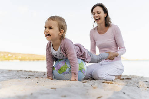 Mutter und kleine Tochter spielen zusammen mit Erde Strand Ball am Meer - DIGF08842
