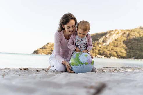 Mother and little daughter looking together at Earth beach ball - DIGF08845