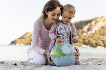Mutter und kleine Tochter schauen gemeinsam auf den Strandball Erde - DIGF08846