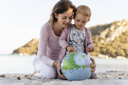 Mother and little daughter looking together at Earth beach ball - DIGF08846