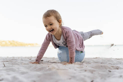 Porträt eines lachenden kleinen Mädchens, das auf einem Strandball aus Erde balanciert - DIGF08850