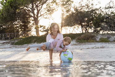 Mutter und kleine Tochter spielen zusammen mit Erde Strand Ball am Meer - DIGF08851