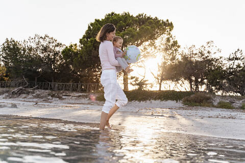 Mutter und kleine Tochter spielen zusammen mit Erde Strand Ball am Meer, lizenzfreies Stockfoto