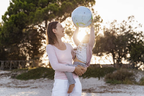 Mother and little daughter playing together with Earth beach ball at sunset - DIGF08853