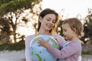 Porträt einer glücklichen Mutter, die zusammen mit ihrer kleinen Tochter einen Strandball auf der Erde betrachtet - DIGF08854