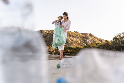 Mutter und kleine Tochter sammeln leere Plastikflaschen am Strand, lizenzfreies Stockfoto