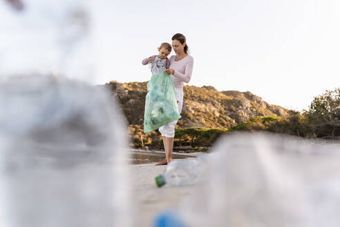 Mutter und kleine Tochter sammeln leere Plastikflaschen am Strand - DIGF08859