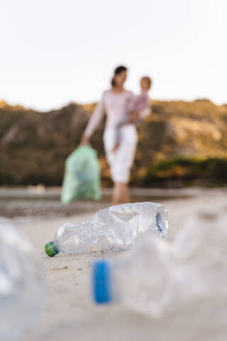 Frau mit Kindern auf dem Arm sammelt leere Plastikflaschen am Strand, lizenzfreies Stockfoto