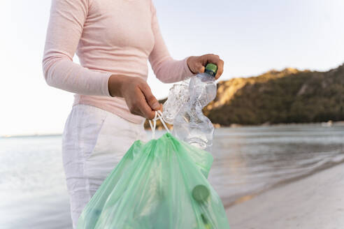 Frau sammelt leere Plastikflaschen am Strand - DIGF08867