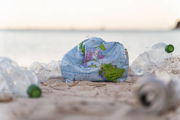 Entleerter Erdstrandball zwischen leeren Plastikflaschen am Strand - DIGF08868