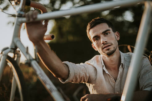 Porträt eines nachdenklichen jungen Mannes mit seinem Fahrrad im Freien - MKF00006