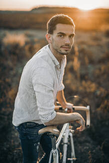 Porträt eines jungen Mannes mit seinem Rennrad im Sonnenschein - MKF00009