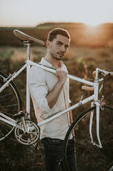 Nachdenklicher junger Mann mit einem Rennrad im Sonnenschein - MKF00011