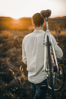 Rückansicht eines jungen Mannes, der ein Rennrad im Sonnenschein trägt - MKF00012