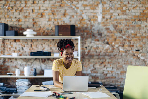 Happy young woman sitting at table with laptop - SODF00114