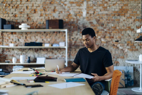 Young man sitting at table taking notes - SODF00118