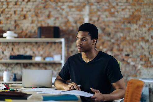 Young man sitting at table thinking - SODF00120