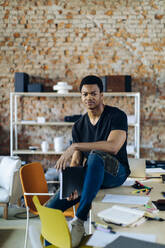 Portrait of confident young man at table in office holding notebook - SODF00125