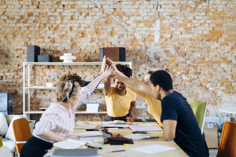 Junge Menschen sitzen zusammen am Tisch und geben sich die Hand, lizenzfreies Stockfoto