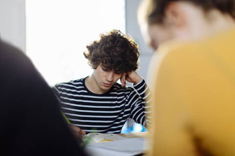 Junge Menschen sitzen zusammen am Tisch und machen sich Notizen, lizenzfreies Stockfoto