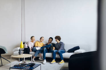 Glückliche junge Leute sitzen zusammen auf der Couch und teilen sich ein Smartphone - SODF00150