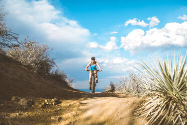 Radfahrerin fährt Mountainbike auf unbefestigtem Weg gegen bewölkten Himmel - CAVF68199