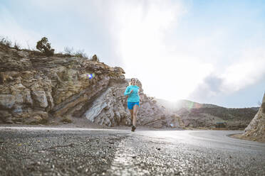 Entschlossene Sportlerin, die an einem sonnigen Tag auf einer Landstraße gegen einen Felsen läuft - CAVF68201