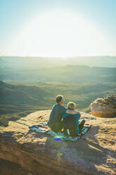 Rear view of couple sitting on mountain during sunny day at Canyonlands National Park - CAVF68203