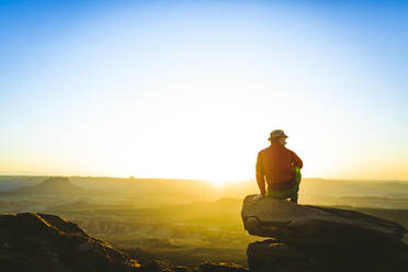 Rear view of male hiker sitting on cliff against sky during sunset at Canyonlands National Park - CAVF68206