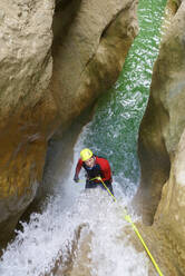 Hochformatige Ansicht eines Wanderers, der beim Canyoning in Aragon am Seil zieht - CAVF68211